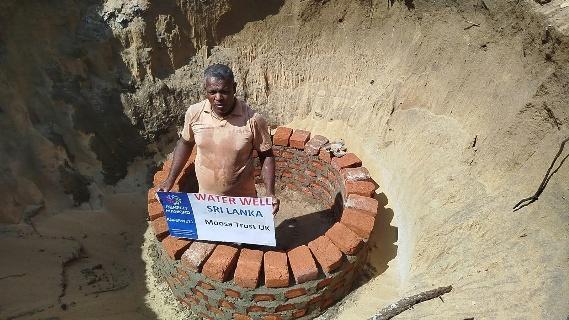 A worker stands inside the excavated pit with the brick lining of the new well in Sallikkelappu, holding the Moosa Trust UK sign