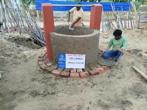 Workers rendering the concrete well head and building its red support pillars during construction in Sallikkelappu
