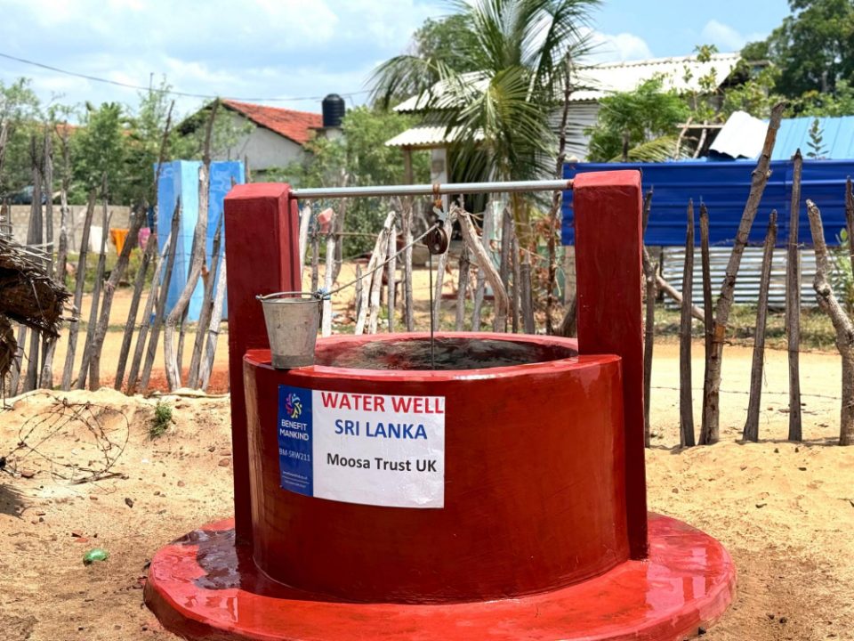 The completed red water well with its pulley, bucket and 'Water Well Sri Lanka, Moosa Trust UK' sign